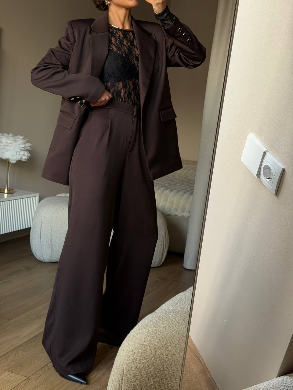 Person wearing a brown suit standing in a room with a mirror reflection.