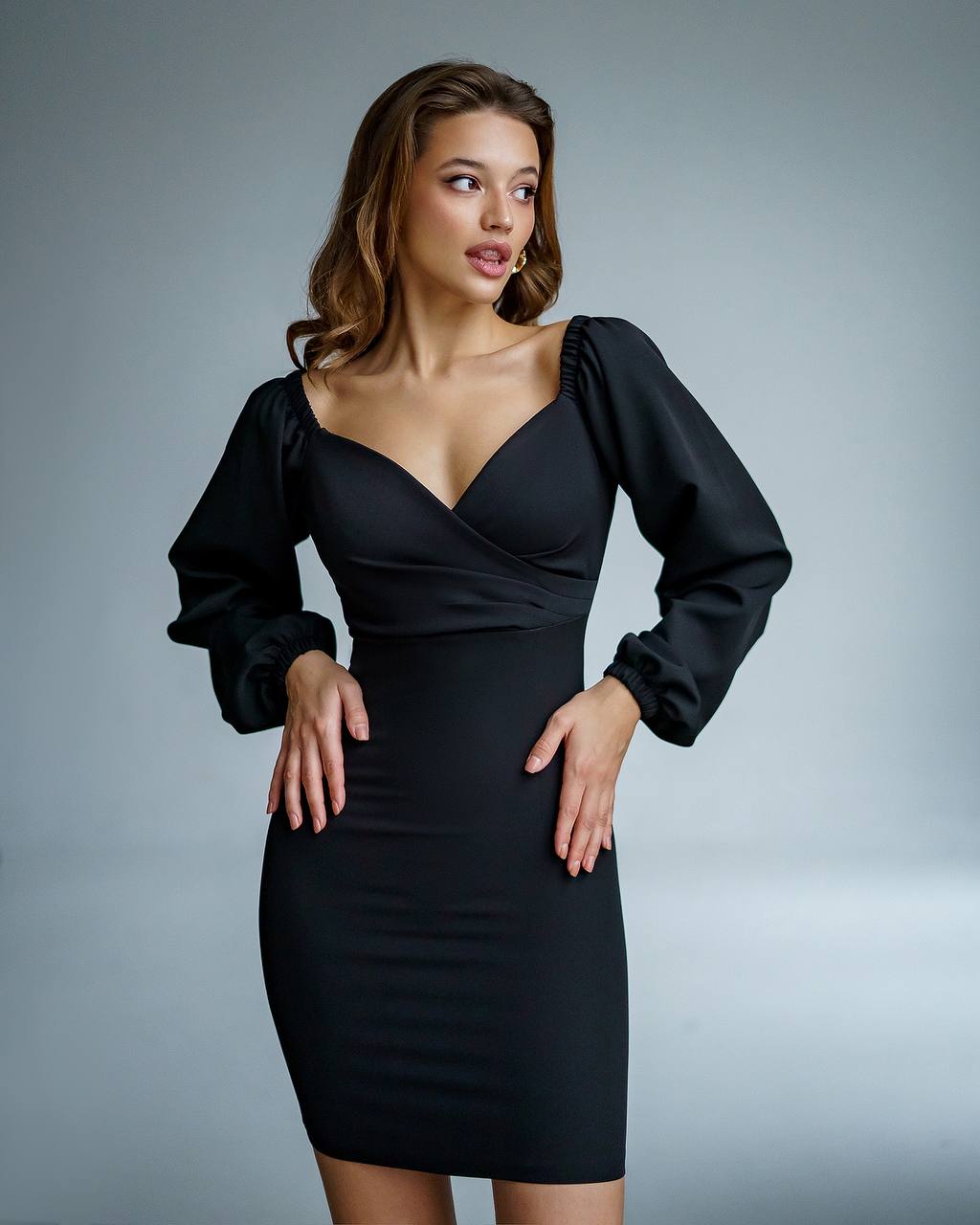 Woman wearing a black dress with long sleeves against a gray background