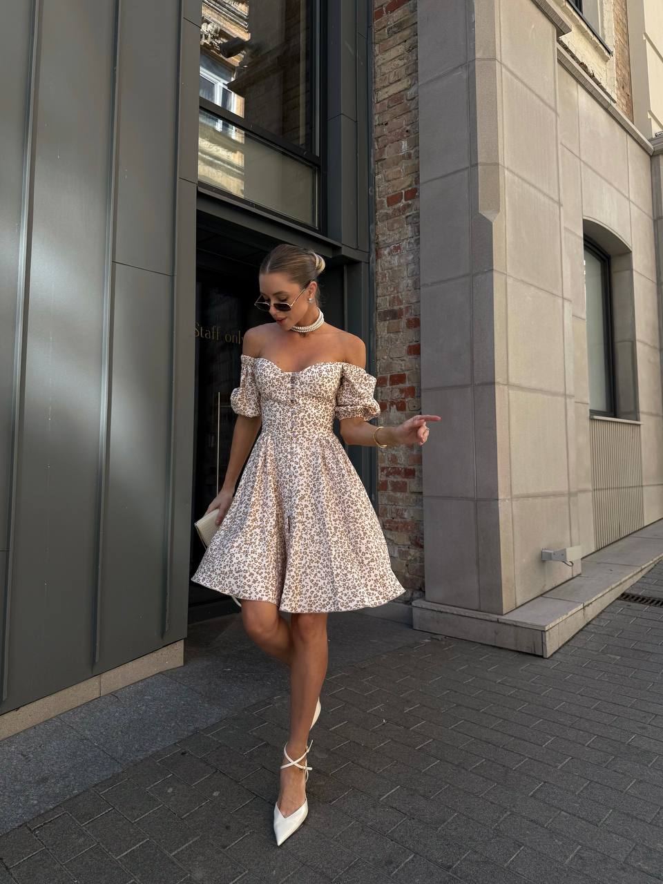 Woman in a floral off-shoulder dress standing on a city street.