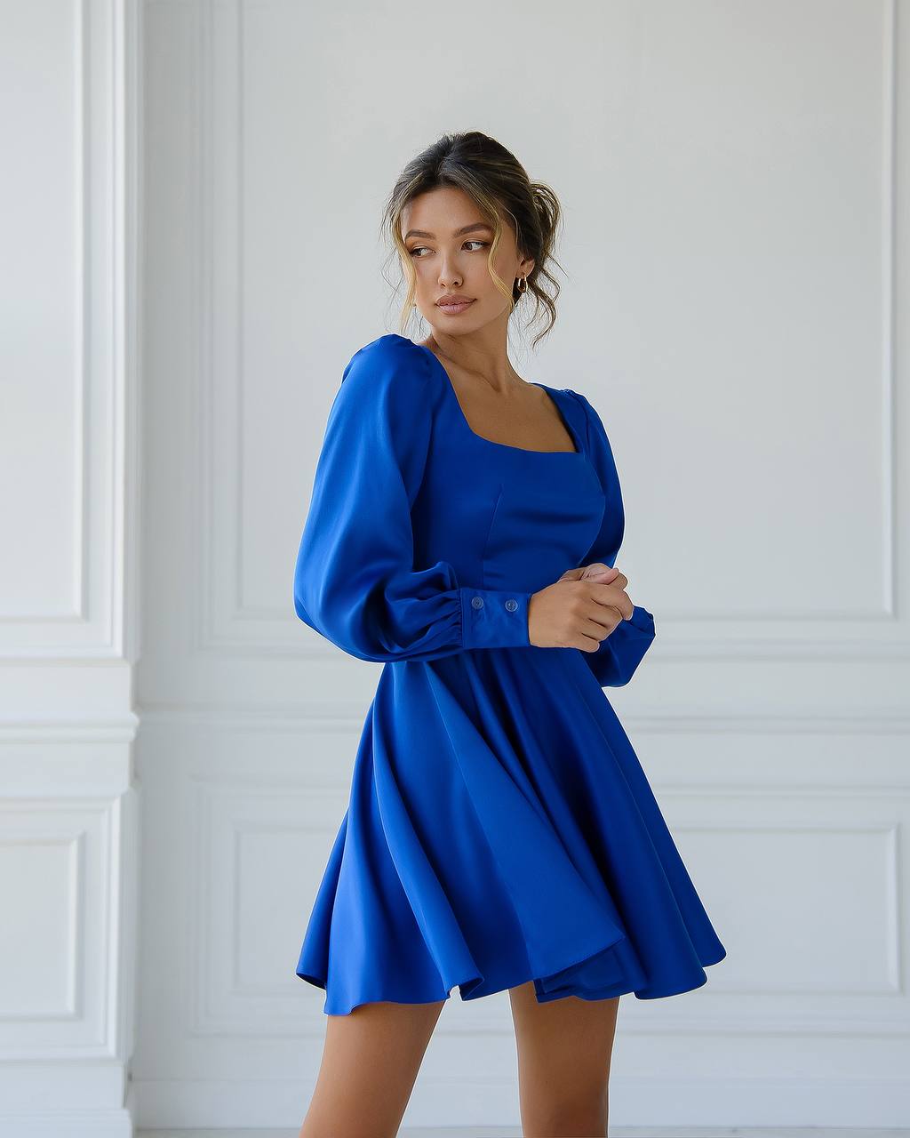 Woman wearing a blue dress against a white wall