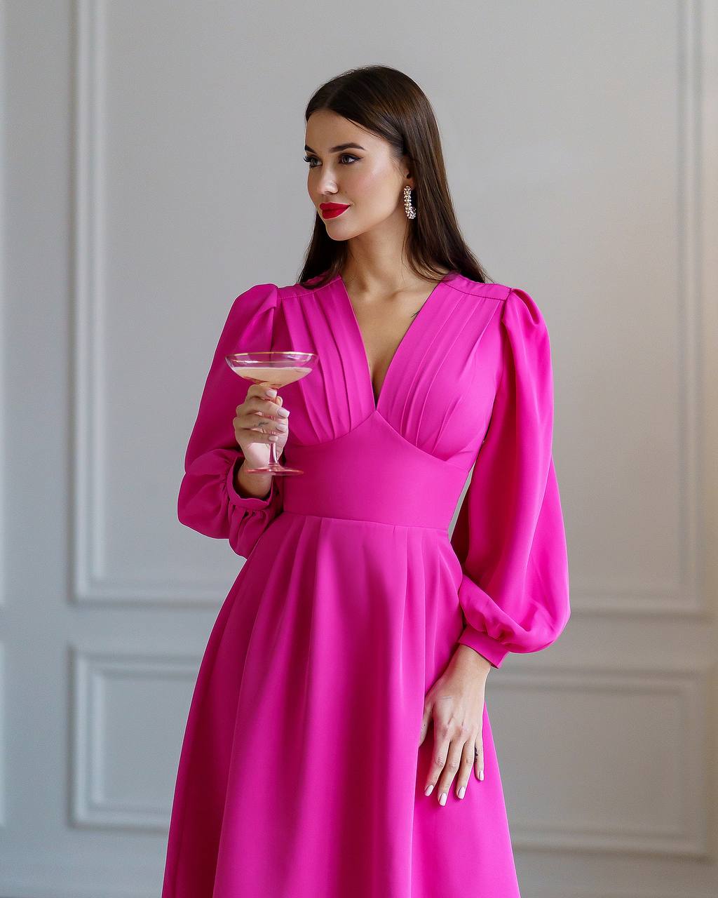 Woman in a bright pink dress holding a glass against a neutral background