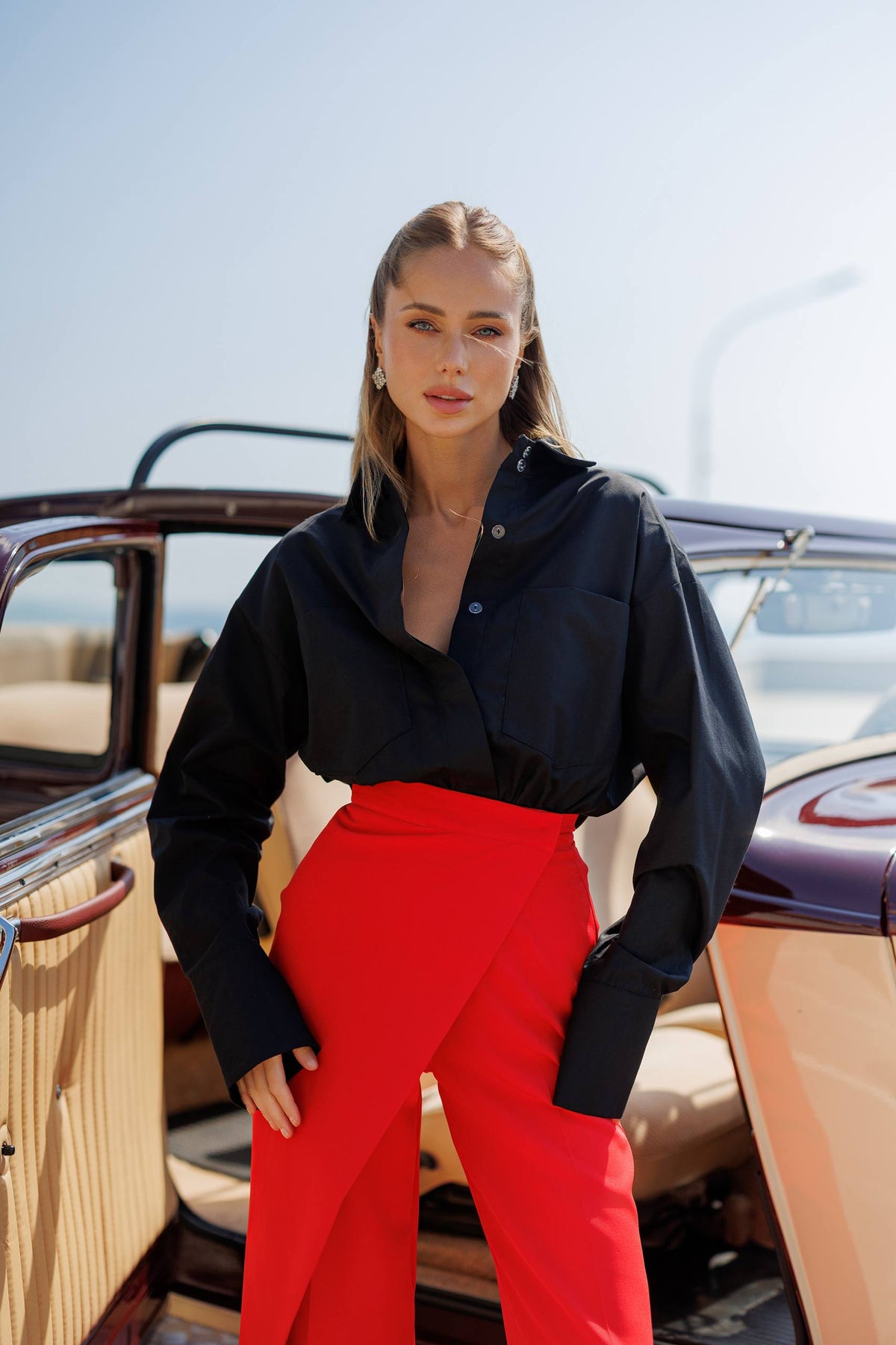 Woman in black shirt and red pants standing next to a vintage car