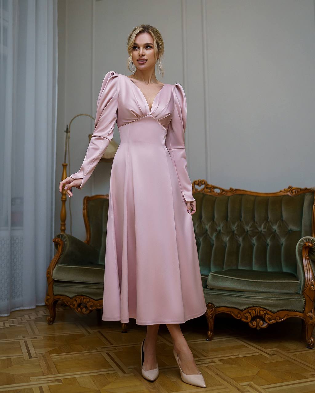 Woman in a pink dress standing in an elegant room with vintage furniture.