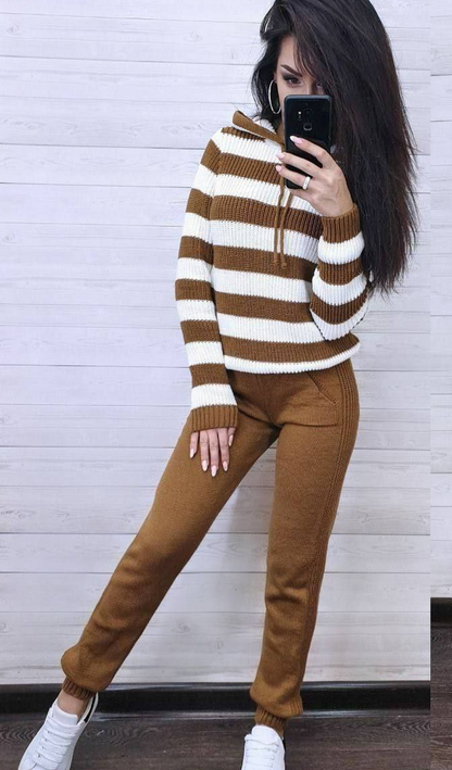 Woman taking a mirror selfie wearing a striped sweater and brown pants against a white wall.