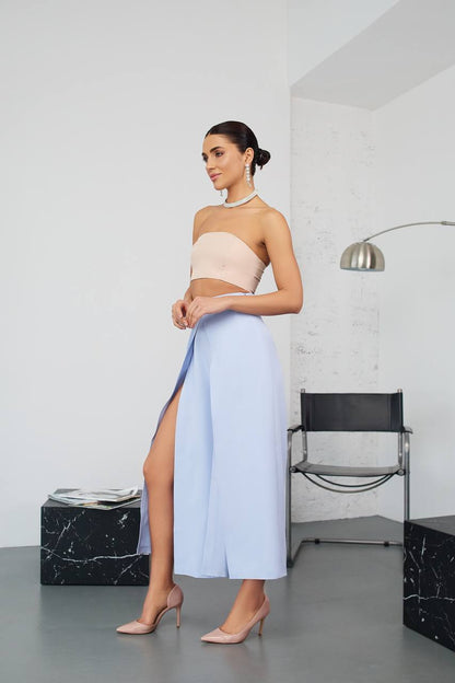 Woman wearing a strapless top and light blue skirt with a high slit in a modern room.