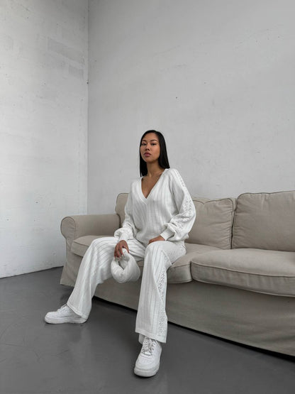Woman in a white outfit sitting on a beige sofa against a plain wall.
