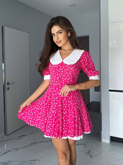 Woman wearing a pink dress with white collar and trim in a modern interior setting