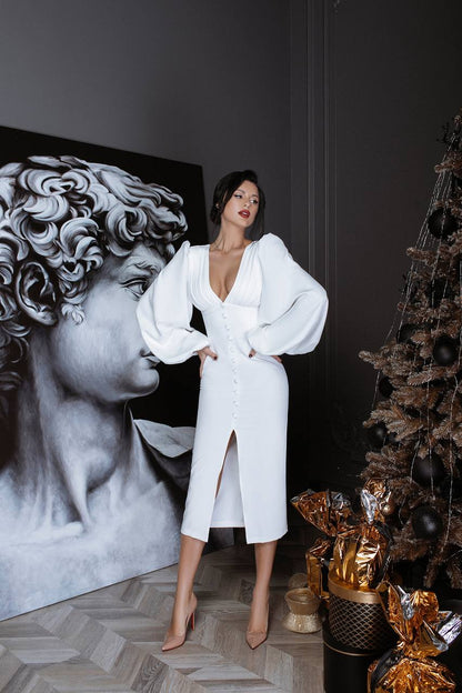 Woman in a white dress standing in a room with a classical sculpture and decorative Christmas tree.