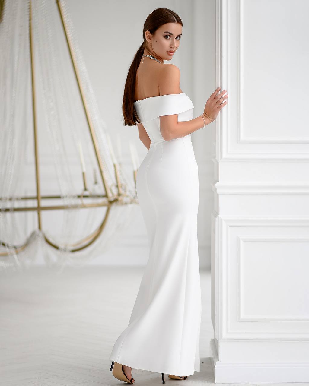Woman in a white off-shoulder gown standing in a minimalistic room.