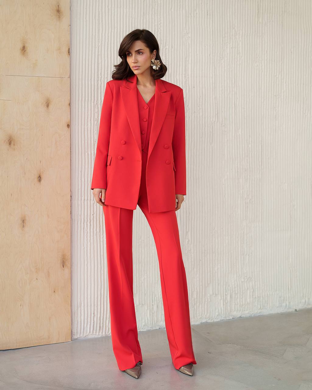 Woman wearing a red suit standing against a neutral wall.
