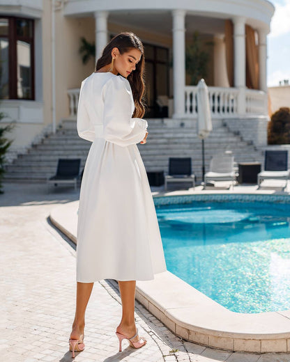 Woman in a white dress standing by a pool with a house in the background