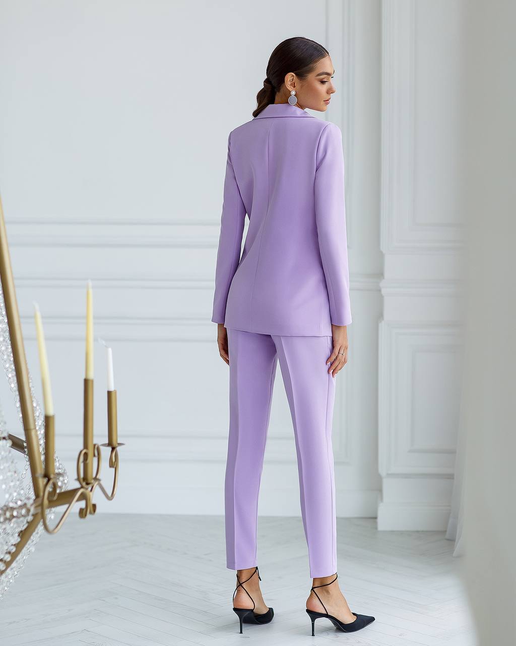 Woman wearing a lavender suit standing in a minimalistic room with white walls and a decorative candle holder.
