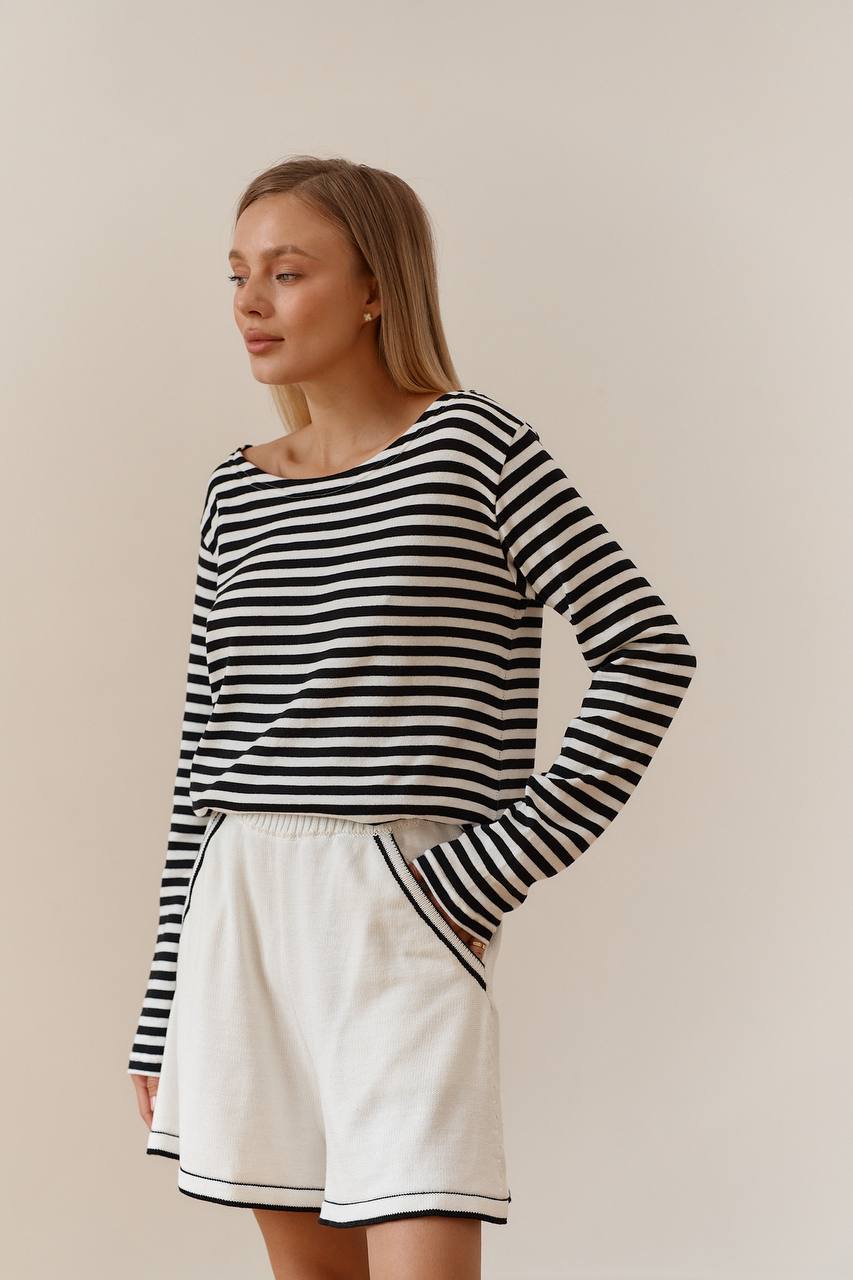 Woman wearing a black and white striped sweater and white shorts against a plain background