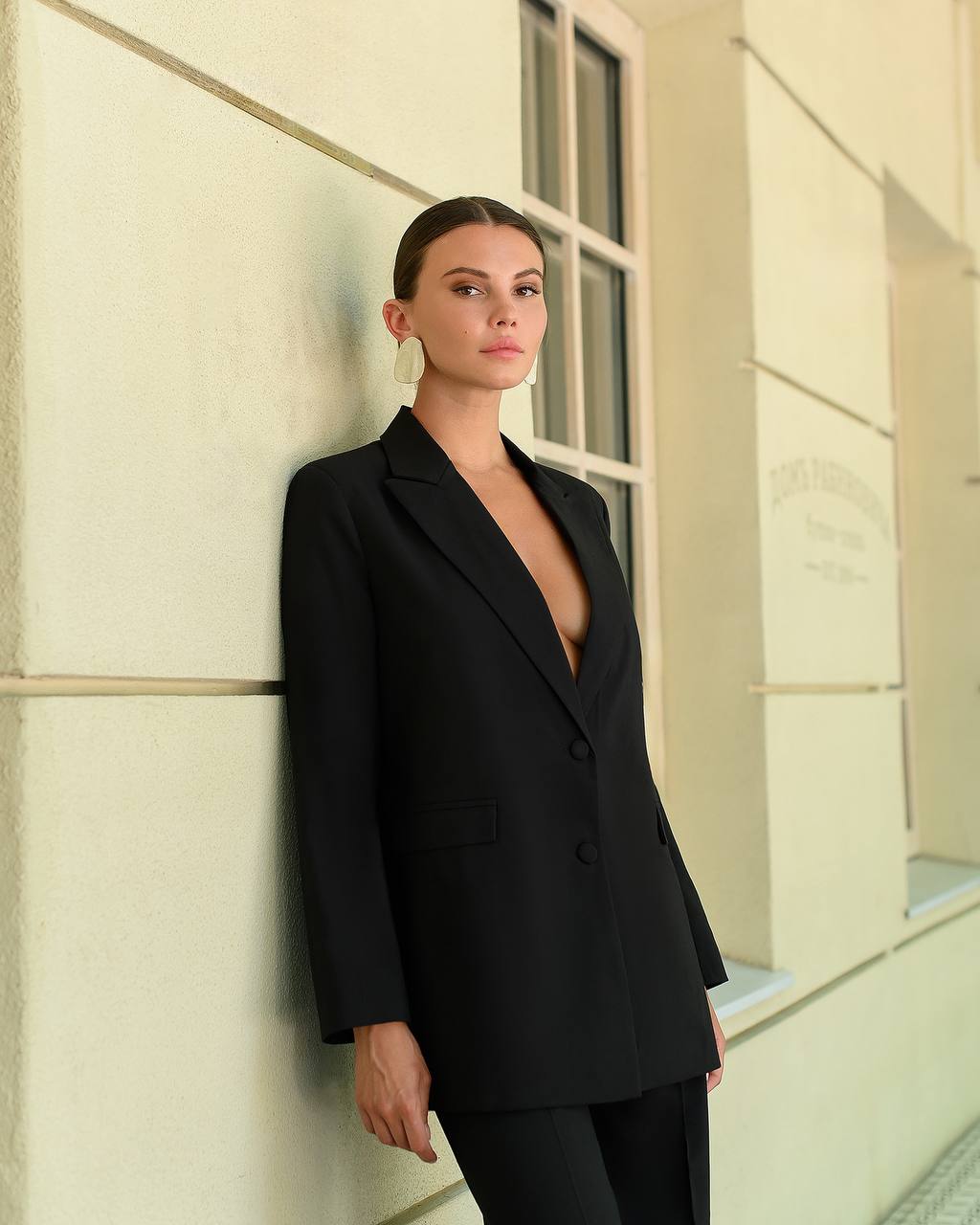 Woman wearing a black suit against a light-colored wall.