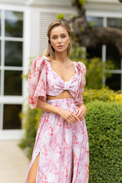 Woman wearing a pink floral dress standing outdoors with greenery in the background