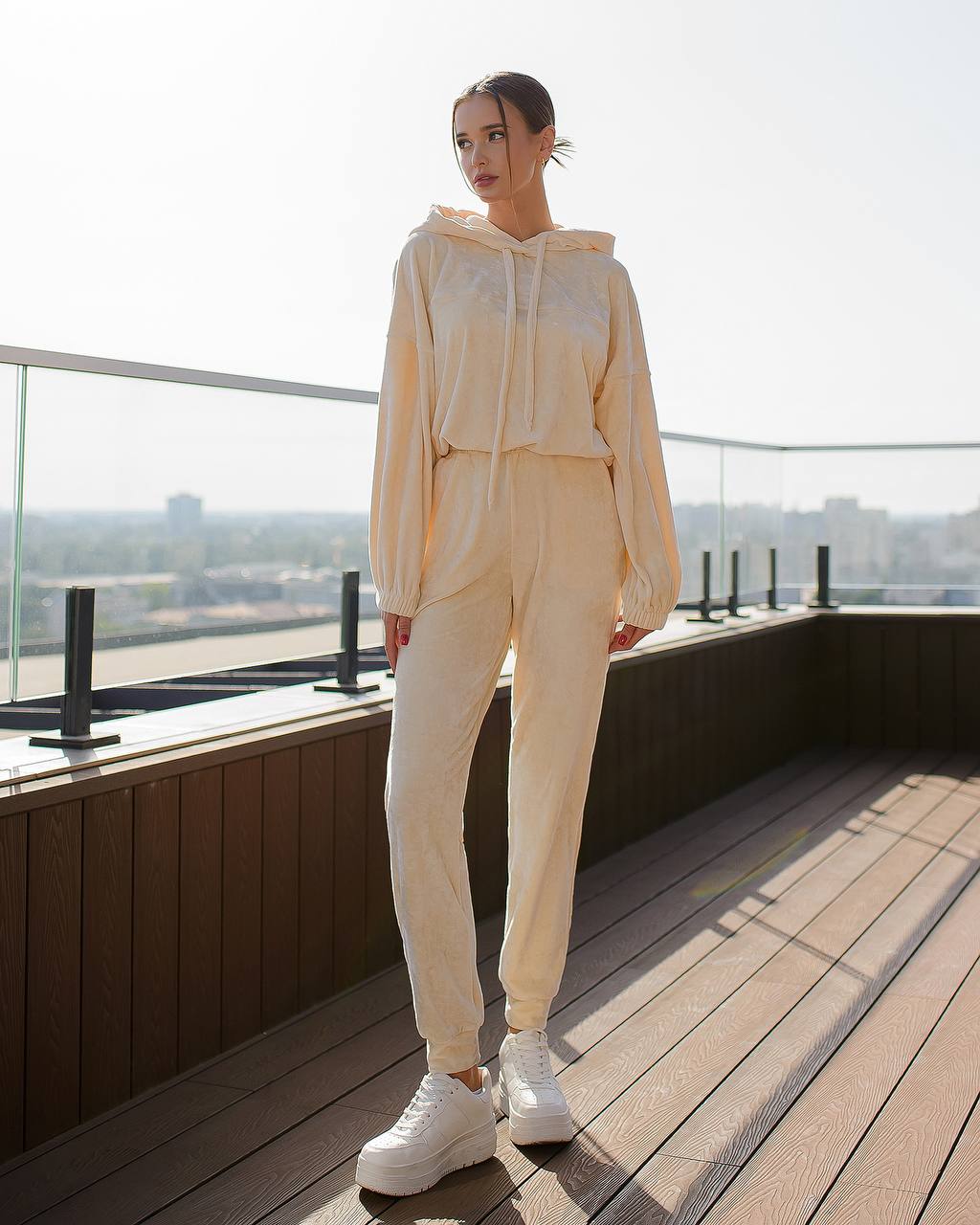 Person wearing a beige tracksuit on a rooftop with a cityscape view.