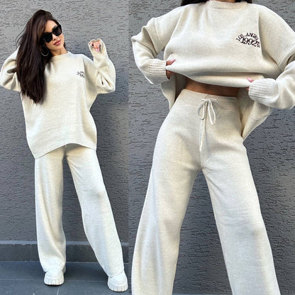 Woman wearing a beige sweater and pants set against a gray wall.