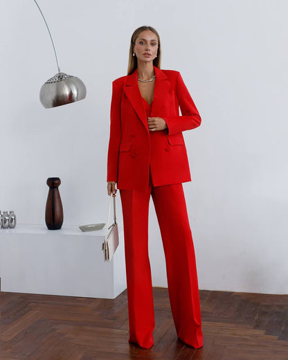 Woman in a red suit standing in a minimalistic room with a white wall and wooden floor.