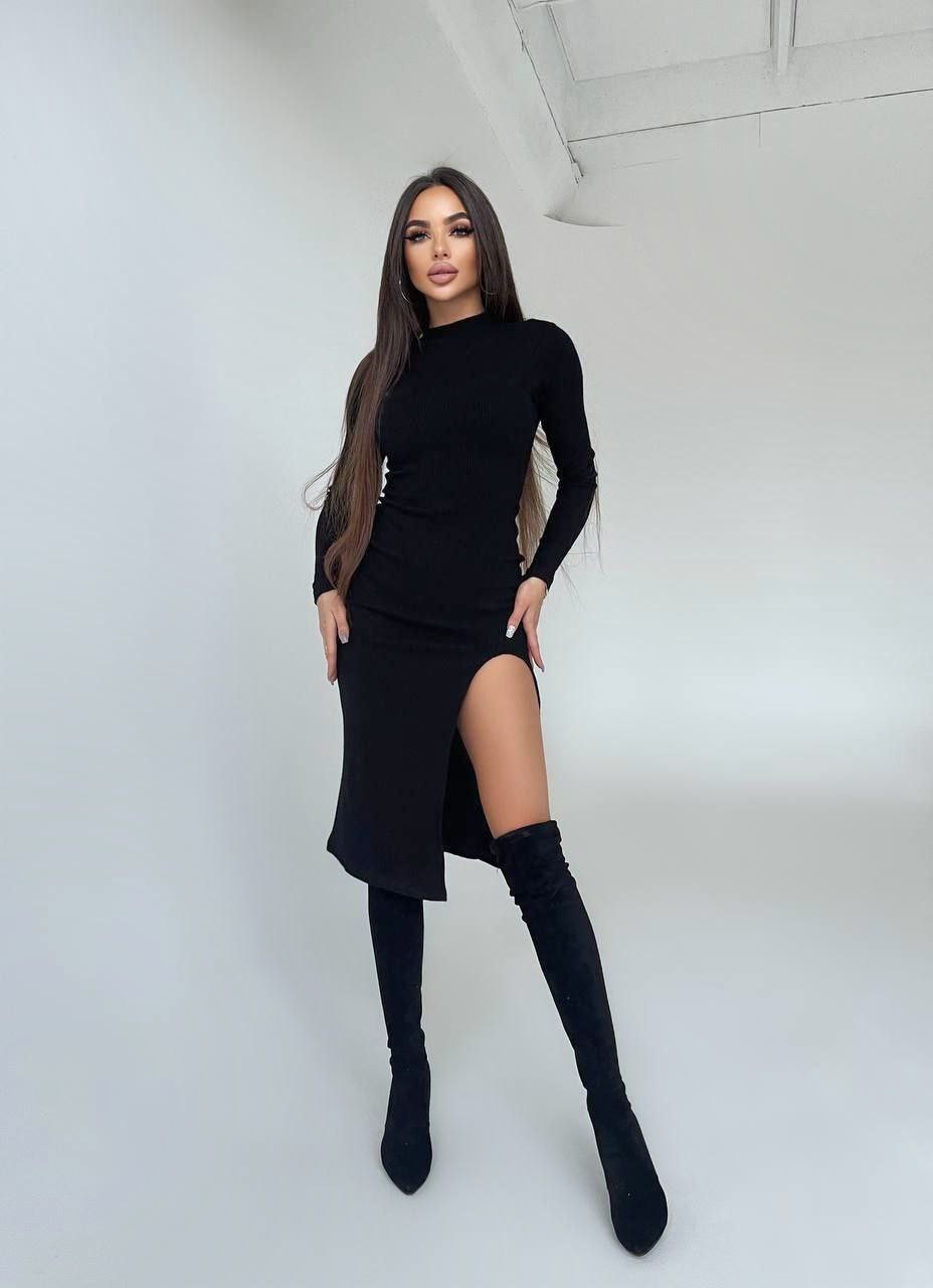 Woman wearing a black dress with a slit and black knee-high boots against a white background