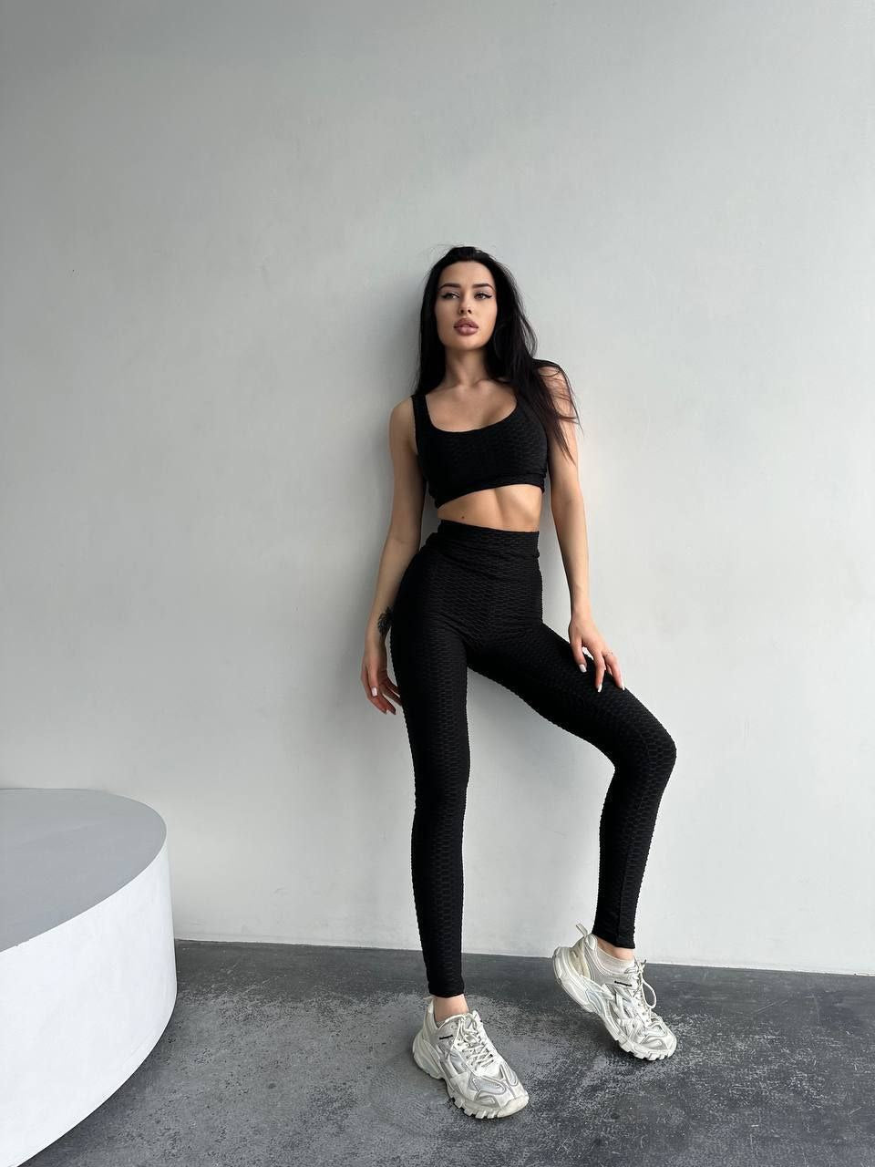 Woman wearing black athletic wear posing against a gray wall.