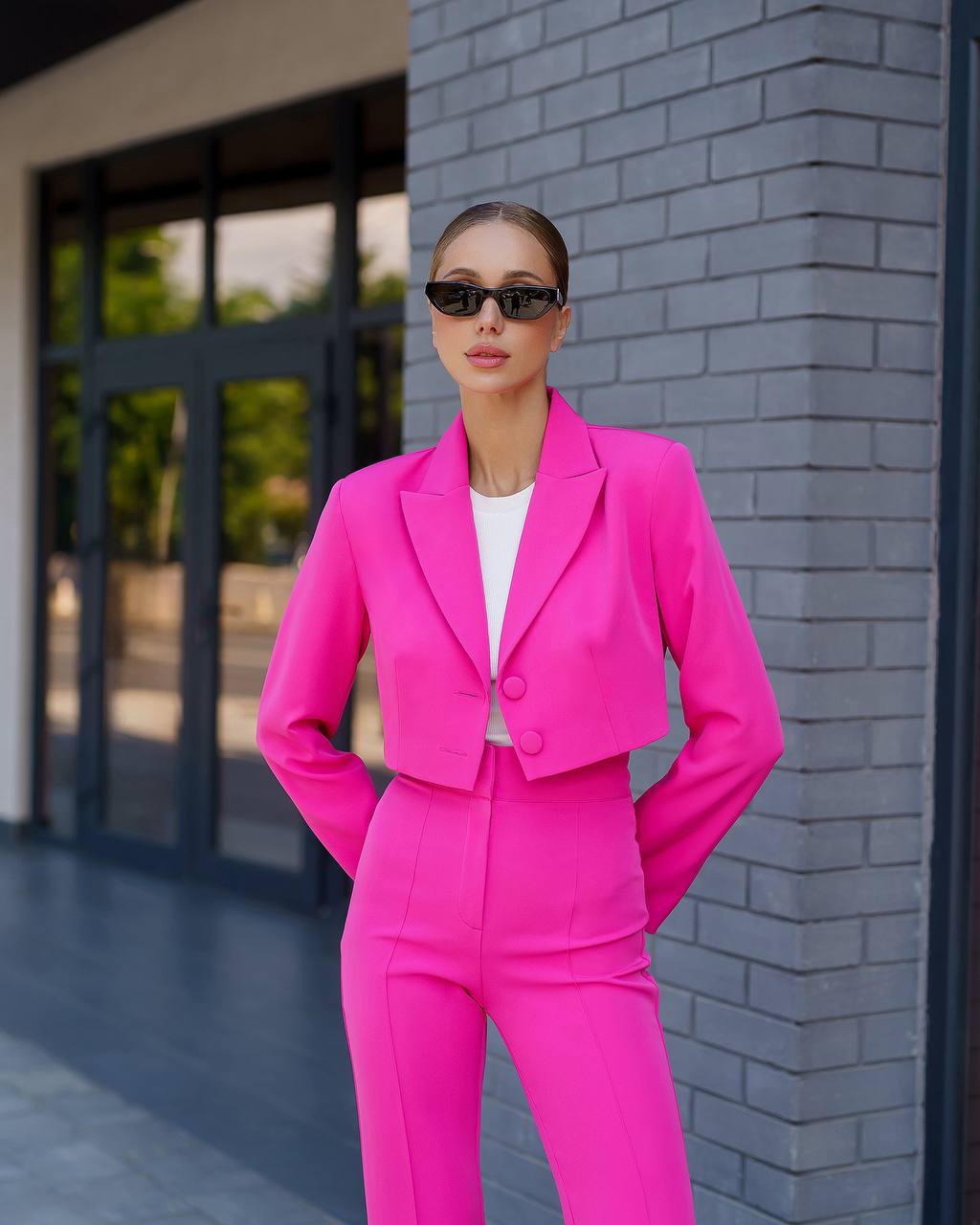 Person wearing a bright pink suit standing against a gray brick wall.