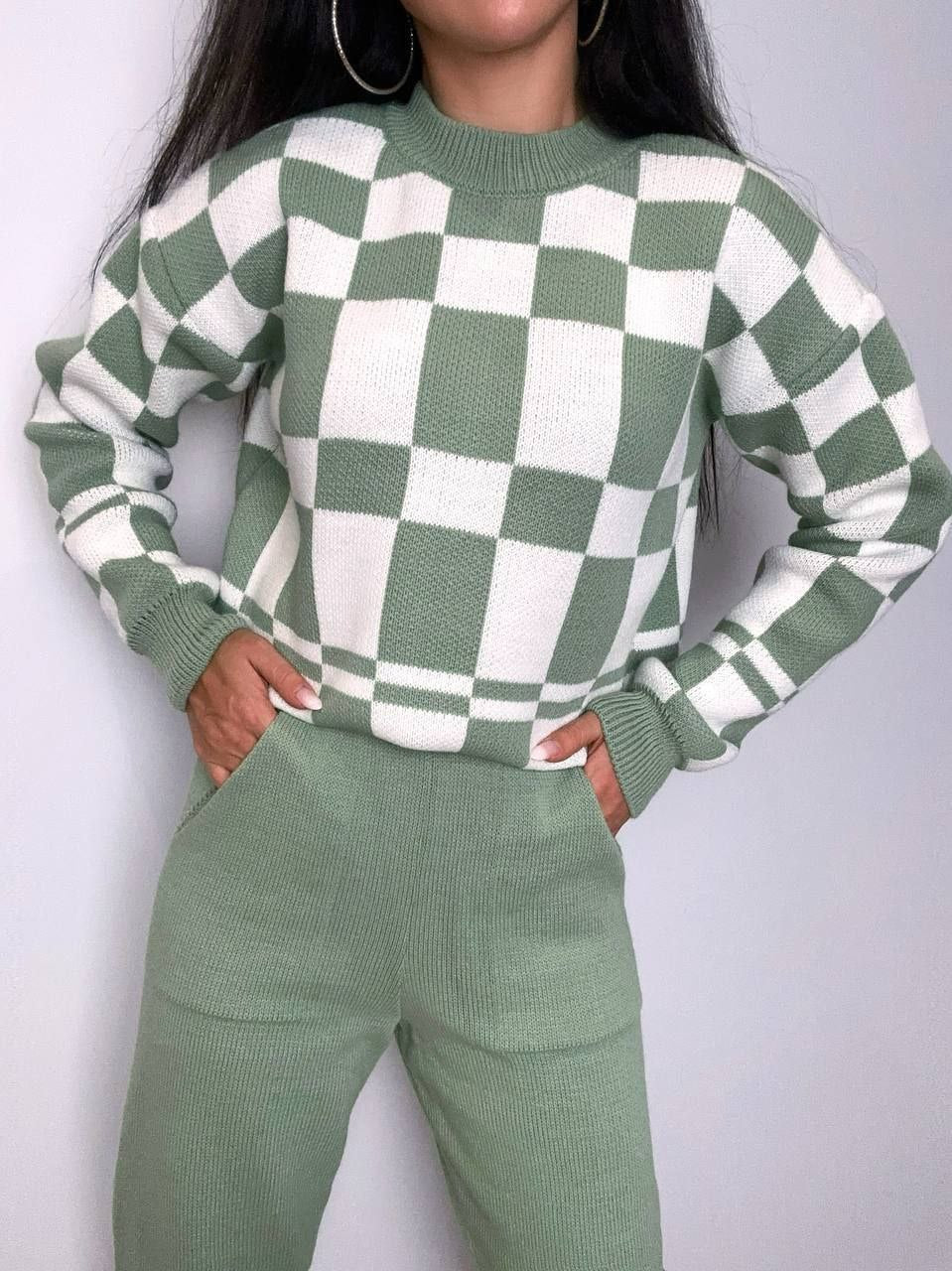 Person wearing a green and white checkered sweater with matching pants against a plain background