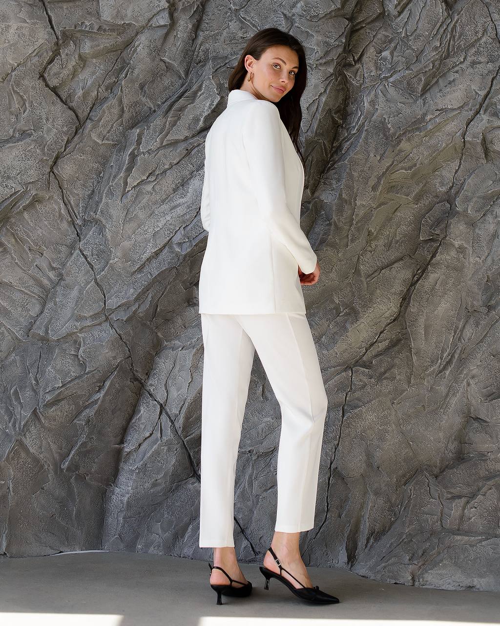 Woman in a white suit standing against a textured gray wall