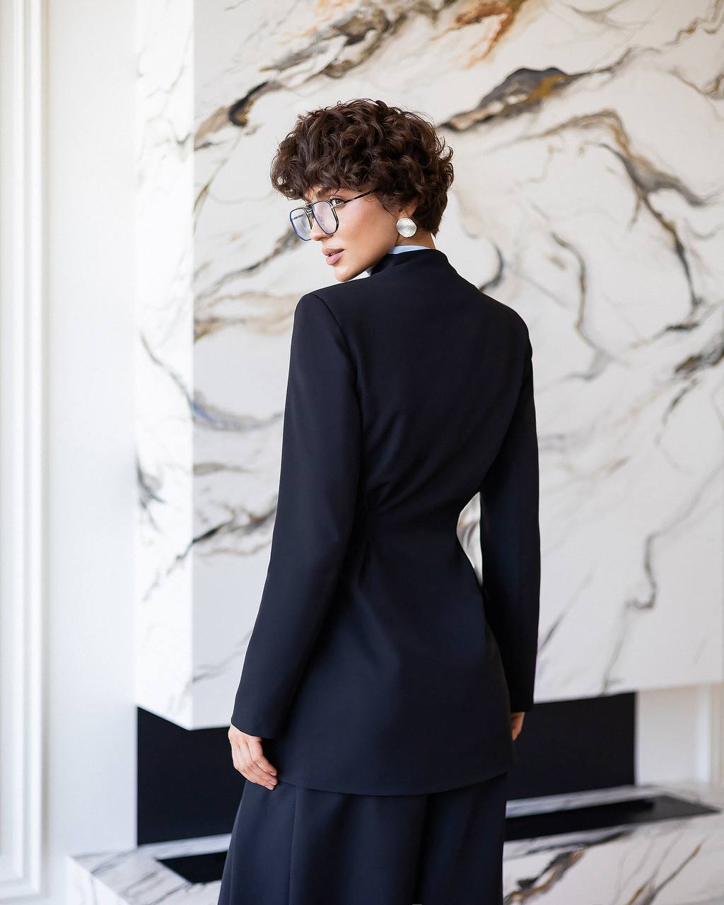 Woman in a navy suit standing in front of a marble wall.