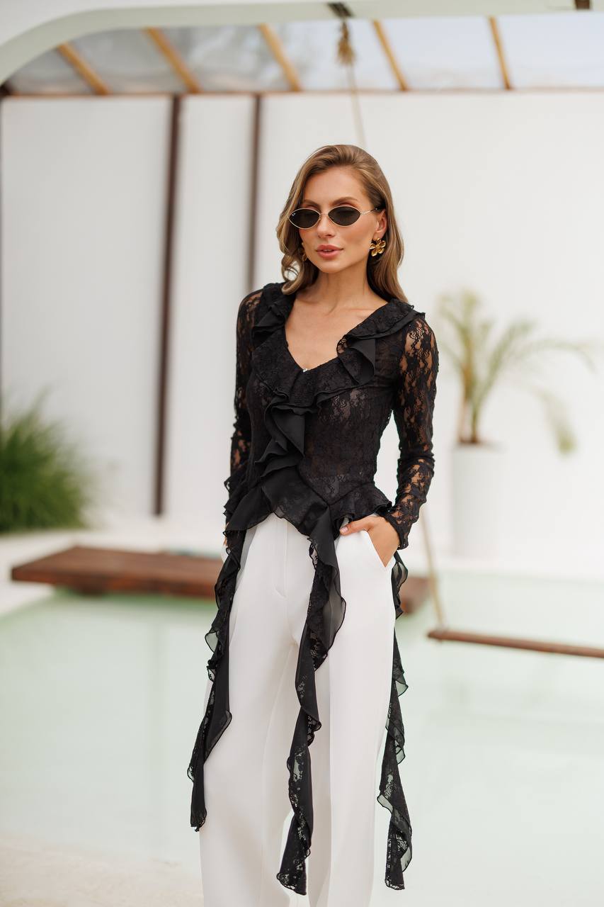 Woman wearing a black lace cover-up and white pants outdoors.