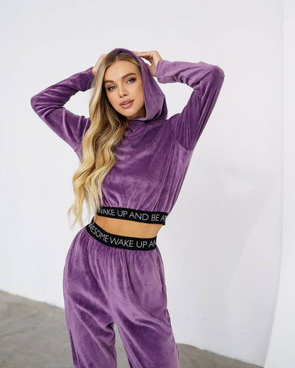 Woman wearing a purple velour tracksuit with text on the waistband against a white background