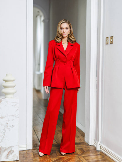 Woman wearing a red suit standing in a well-lit room with white walls and wooden floor.
