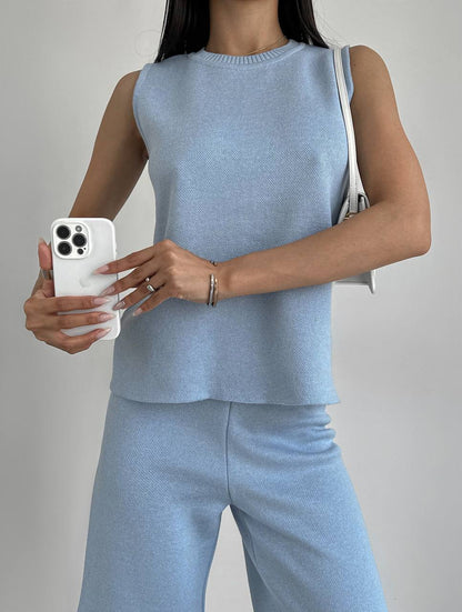 Person wearing a light blue sleeveless top and pants, holding a phone with a gray background