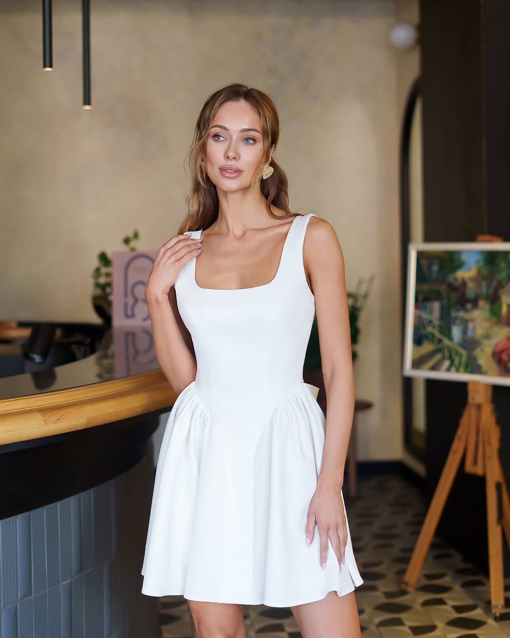 Woman in a white dress standing in an indoor setting with decor elements.