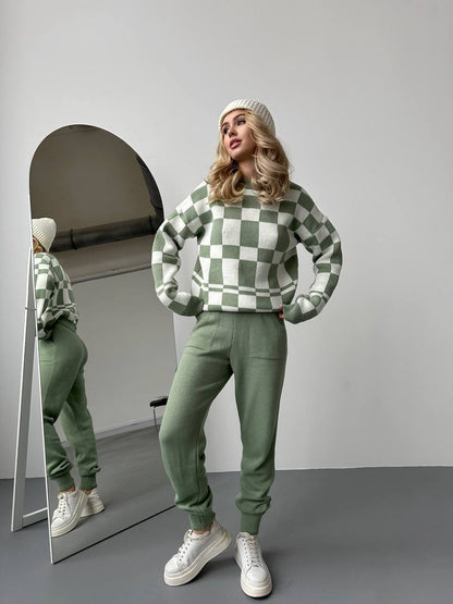 Woman in a green checkered sweater and pants standing in front of a mirror.