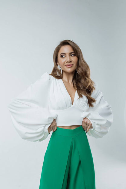 Woman wearing a white blouse with wide sleeves and green pants on a light gray background
