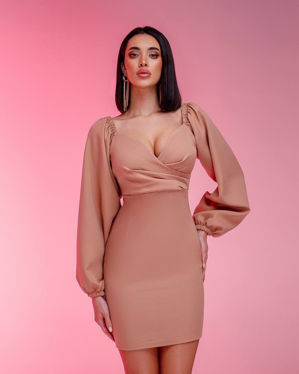Woman wearing a beige dress with long sleeves on a pink background