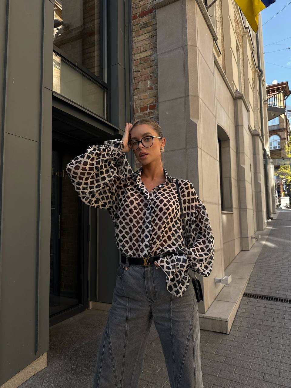 Woman wearing a leopard print blouse and jeans standing on a city street.