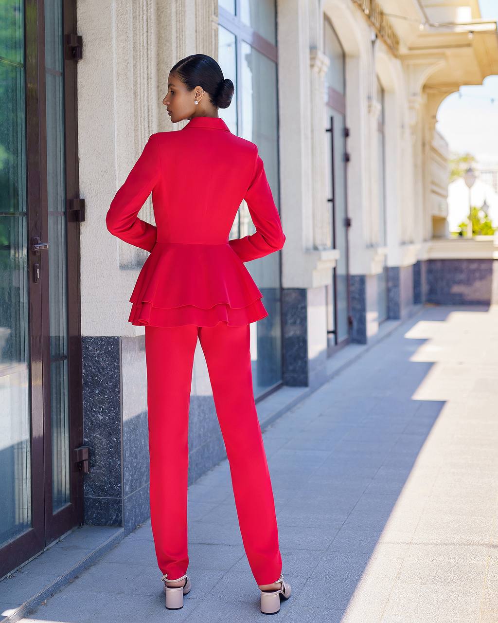 Woman in a red suit standing on a sidewalk with a building in the background