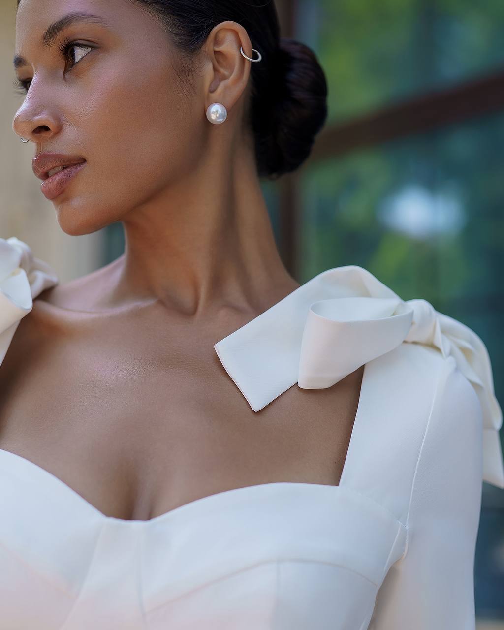 Woman wearing a white dress with a large bow on her shoulder, outdoors.