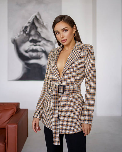 Woman wearing a checkered blazer with a belt in an indoor setting.