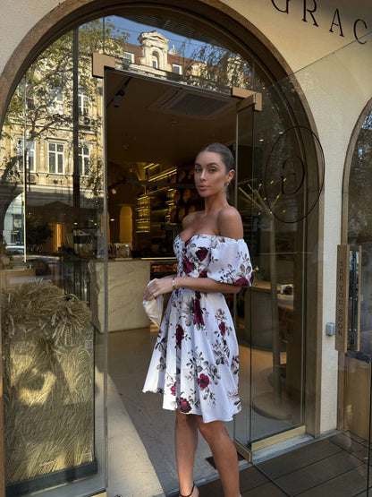 Woman in a floral dress standing in front of a store entrance.