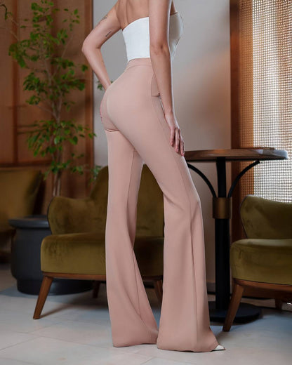 Person wearing beige flared pants in a room with green chairs and a plant.