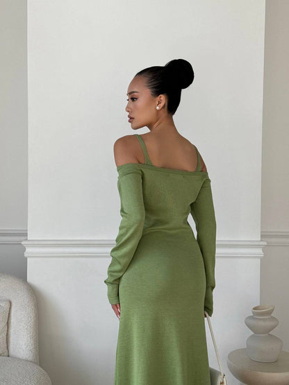Woman in a green dress standing in a room with white walls and a chair.