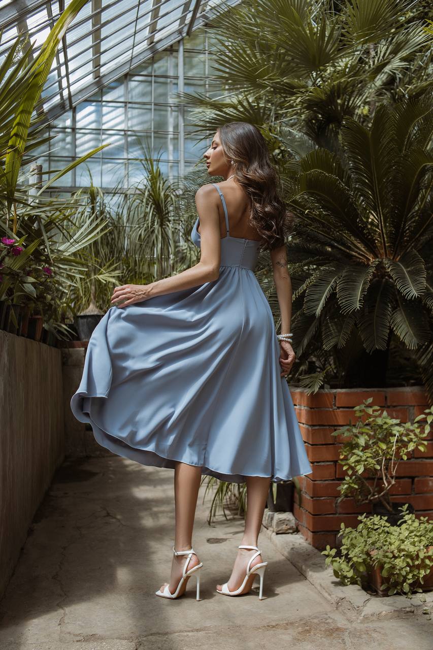 Woman in a light blue dress standing in a greenhouse with plants around.