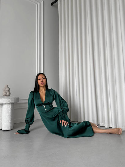 Woman in a green dress sitting on the floor against a white curtain.
