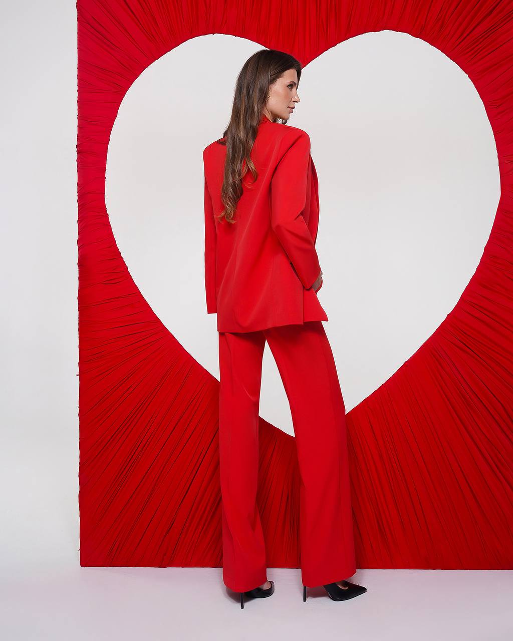 Woman in a red suit standing in front of a heart-shaped red and white wall.