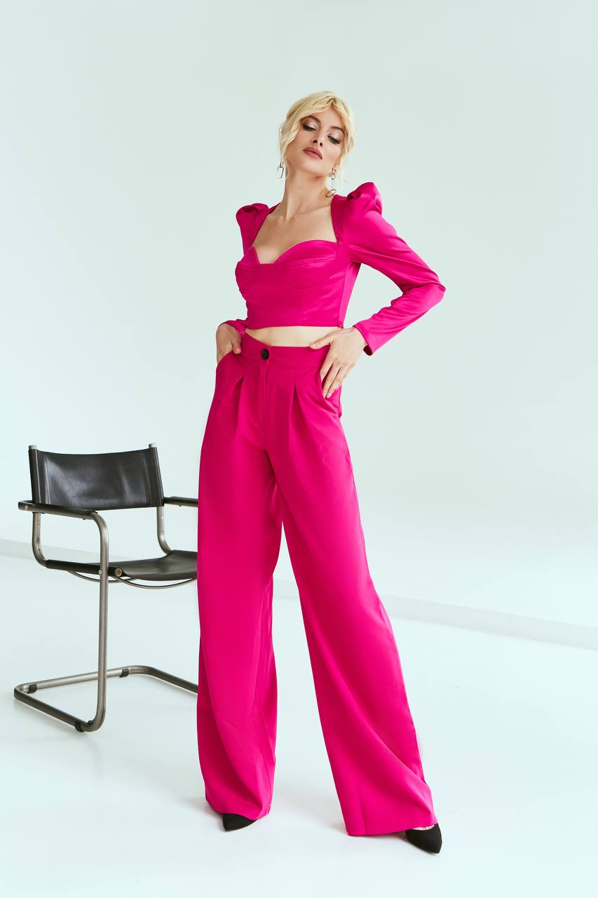 Person wearing a bright pink outfit with high-waisted pants and a top, standing against a white background.