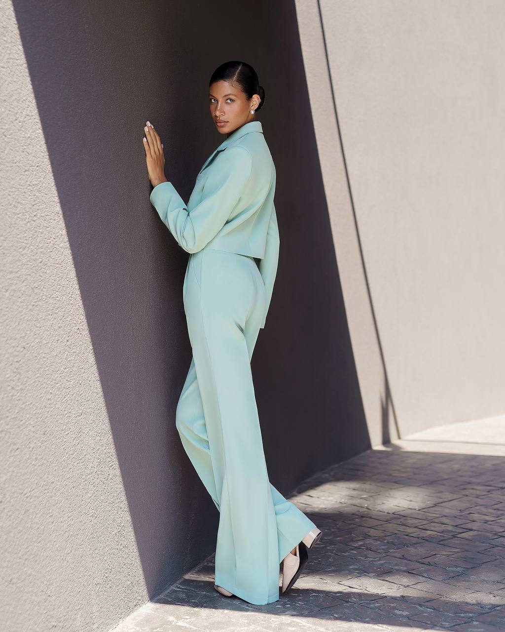 Woman in a light blue suit standing against a textured wall.