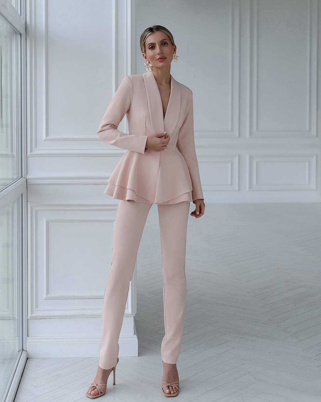 Woman wearing a pink suit standing in a room with white walls.