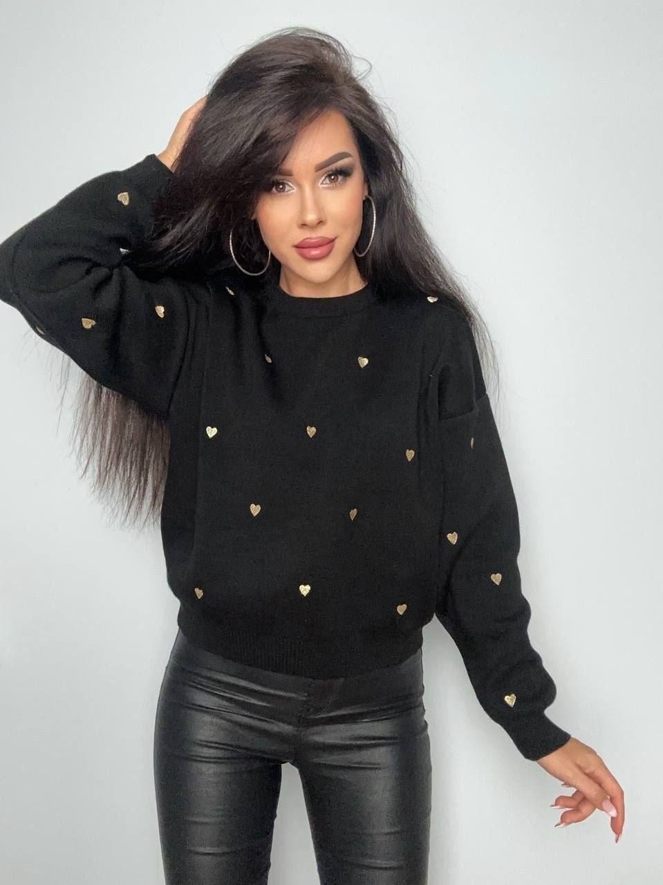 Woman wearing a black sweater with gold heart patterns against a white background